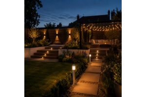 Landscaped UK garden at dusk with stainless steel bollard lights, round recessed step lights, up/down wall lights and warm string lighting creating a layered outdoor lighting design around a modern patio and garden path.