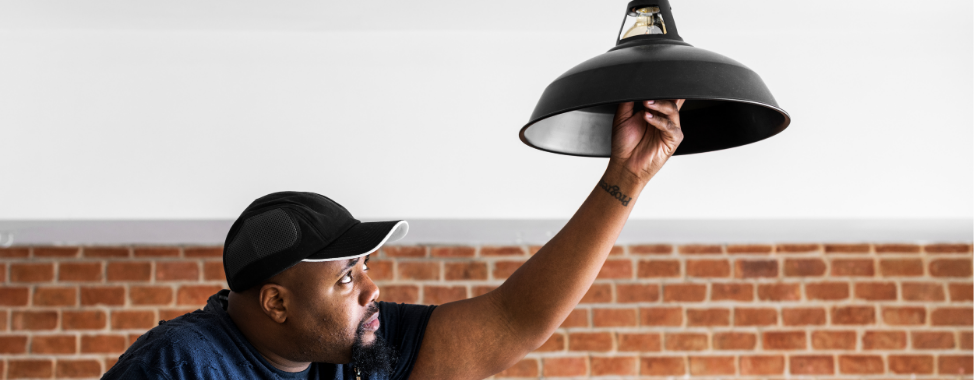 A man standing on a ladder fixing a flickering ceiling light with his hand on the light