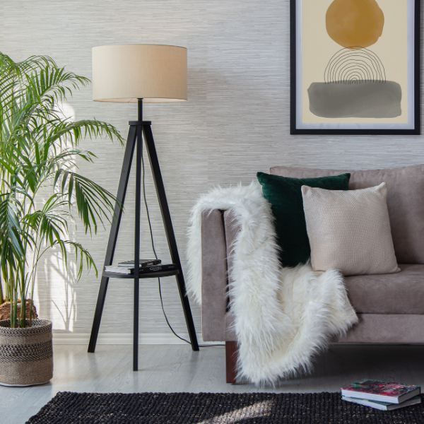 Scandi style living room with a tripod floor lamp next to a sofa that has cushions and a fur throw on it